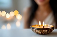 Decorative aromatic candle in ornate metal holder with warm glowing flame against blurred bokeh background creates peaceful ambiance for spa and meditation.