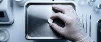 Gloved hand touching digital tablet screen in sterile medical or laboratory environment, suitable for healthcare technology and clinical applications.