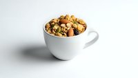 Healthy trail mix with nuts, dried fruits and seeds in white ceramic cup on clean background for snacking and nutrition concepts.