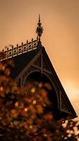 Victorian gingerbread house detail with ornate ironwork and decorative trim silhouetted against warm golden sunset sky creating romantic architectural mood.