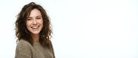 Young woman with wavy brunette hair and warm smile wearing neutral beige sweater, isolated on white background for portrait and lifestyle design use.