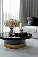 Elegant living room interior with black and gold coffee table featuring white hydrangea bouquet, books, and decorative elements against soft gray curtains and sofa.