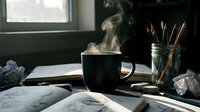 Steaming black coffee mug on a cluttered creative desk with sketchbook, pencils in a jar, and crumpled paper in moody light.