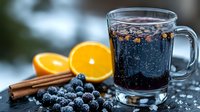 Hot mulled wine with fresh blueberries, orange slices and cinnamon sticks on wooden table. Warming winter beverage for cold weather celebrations and holidays.