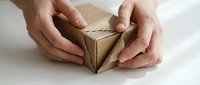 Hands carefully protecting small brown paper package tied with natural twine string on white surface for shipping and delivery concepts.