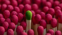 Single green match head standing out among numerous red match heads, symbolizing individuality, uniqueness, and contrast in a uniform environment.