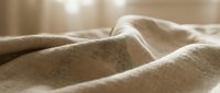 Closeup of soft beige linen fabric with natural texture and gentle folds, suitable for home decor, textile design, and interior styling projects.
