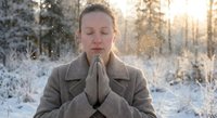 Peaceful woman meditating outdoors in snowy winter forest with warm sunlight creating serene atmosphere for mindfulness and spiritual wellness practices.