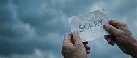 Hands holding torn paper with sorry message against dramatic cloudy sky background expressing apology regret forgiveness reconciliation emotional healing.