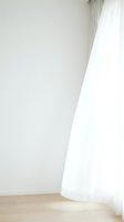 Sheer white curtain flowing against neutral wall with wooden floor, creating minimalist interior design aesthetic for home decor and architectural visualization projects.