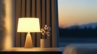 Modern table lamp with warm light creates cozy evening ambiance in contemporary living room with mountain view through large window at sunset.