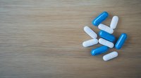 Blue and white capsule pills scattered on wooden surface with copy space for medical or pharmaceutical content. Medical treatment concept.