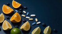 Fresh citrus fruits orange lemon lime wedges with blueberries and vitamin pills on dark blue background for healthy nutrition supplement concept.