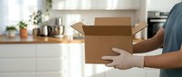 Man in gloves holding open cardboard box in modern kitchen during home moving or delivery service. Relocation and shipping concept for residential use.