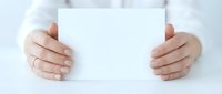 Caucasian woman holding blank white card or paper in both hands, wearing white shirt, closeup view of hands and torso for business communication, marketing, and advertising purposes.