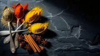 Aromatic spices in vintage spoons on dark slate background. Turmeric, paprika, coriander seeds and cinnamon sticks for culinary cooking and seasoning.