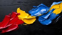 Vibrant red, yellow and blue oil paint strokes on black textured background create dynamic abstract composition with thick impasto technique showing artistic expression.