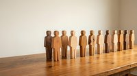 Wooden figurines in gradient from dark to light brown standing in a row on wooden table, representing diversity, teamwork, and human resources concepts.
