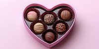 Assorted luxury chocolate truffles in pink heart-shaped box on pink background, romantic Valentine's Day gift or sweet dessert presentation.