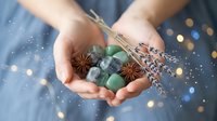 Cupped hands holding winter spices star anise cinnamon eucalyptus lavender with magical bokeh lights and falling snow creating festive holiday atmosphere.