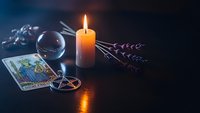 Mystical fortune telling setup with tarot cards, crystal ball, burning candle and lavender sprigs on dark surface for spiritual guidance and divination.