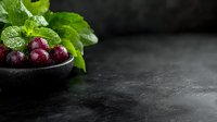 Fresh red grapes with green mint leaves in dark bowl on black stone surface with water droplets for culinary and beverage photography.
