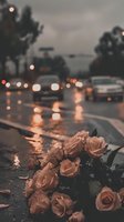 Bouquet of roses lying on wet asphalt road during rainy evening with blurred traffic lights and vehicles in background, conveying loss, remembrance, and emotional moments.
