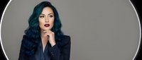 Professional businesswoman with blue hair in dark suit posing thoughtfully against gray background for corporate branding and marketing materials.