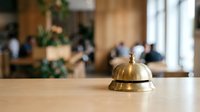Golden brass service bell on wooden hotel reception desk with blurred lobby background for hospitality and customer service concepts.