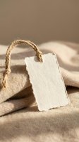 Blank cotton fabric tag with natural jute rope string on beige linen textile background for eco-friendly branding and sustainable fashion labels.