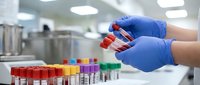 Medical laboratory technician in blue gloves holding blood sample tubes for testing and analysis in modern clinical research facility.