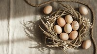 Fresh brown eggs nestled in woven basket with wheat stalks and rope on rustic burlap fabric. Organic farm produce concept for cooking and baking projects.