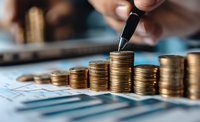 Male hand stacking gold coins on financial documents showing growth chart, representing investment strategy, savings increase and wealth management concept.