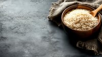 Raw white rice in rustic wooden bowl with wooden spoon on dark concrete background with brown linen napkin, copy space for menu or recipe.