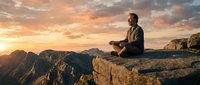 Middle-aged Caucasian man meditating on mountain cliff edge during golden hour sunset with dramatic orange sky and rugged peaks in background for wellness content.