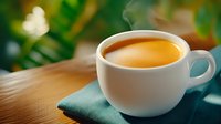 Fresh hot espresso in white ceramic cup on teal napkin against wooden surface with steam rising and blurred green foliage background. Natural morning light setting.