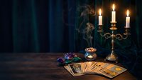 Mystical fortune telling scene with tarot cards spread on wooden table, burning candles in brass candlestick, crystal ball and dark atmospheric background.