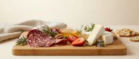 Gourmet charcuterie board with salami, soft cheese, fresh strawberries and rosemary herbs on wooden cutting board for entertaining and appetizers.