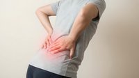 Man in gray shirt touching lower back with red pain highlight showing lumbar discomfort and muscle strain for healthcare and wellness concepts.