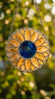 Stained glass sunflower suncatcher hanging on chain with yellow petals and blue center against blurred green foliage background for home decor projects.