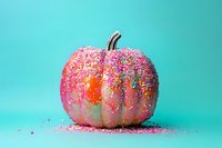Pink painted pumpkin decorated with colorful sprinkles and glitter against turquoise background, creative seasonal holiday concept for Halloween and autumn.