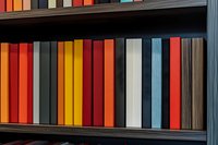 Colorful hardcover books arranged in rows on dark wooden shelf, creating vibrant pattern of orange, red, yellow and blue spines against black background.