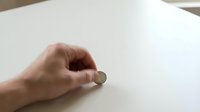 Hand holding small white pill or tablet on clean white surface for medical healthcare pharmaceutical concept.