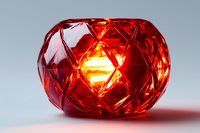 Red crystal glass candle holder with geometric diamond pattern illuminated from within, creating warm ambient glow against light background.