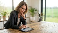 Professional businesswoman with glasses working on tablet in modern office space with natural lighting and plants for corporate presentations.