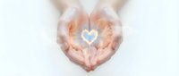 Cupped hands forming heart shape with glowing blue heart symbol inside, representing love, care, protection and compassion on white background.