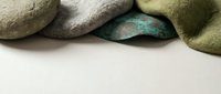 Smooth river stones and aged patina copper piece with soft green fabric on light background, top border composition with copy space.