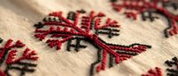 Traditional folk embroidery with red and black cross-stitch floral pattern on beige linen fabric, showcasing ethnic textile craft and handmade heritage design.