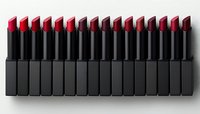 Row of matte black lipstick tubes with vibrant red tips arranged in precise linear formation against white background, creating minimalist makeup composition.