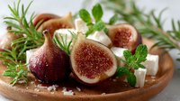Fresh figs with creamy cheese and aromatic herbs on rustic wooden board for gourmet cooking and healthy Mediterranean cuisine recipes.